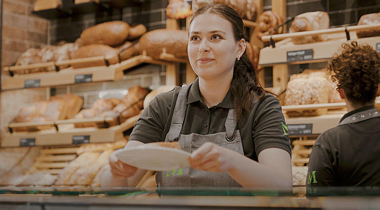 Verkäuferin-Azubi der Bäckerei Meyer arbeitet freundlich an der Brot-Theke