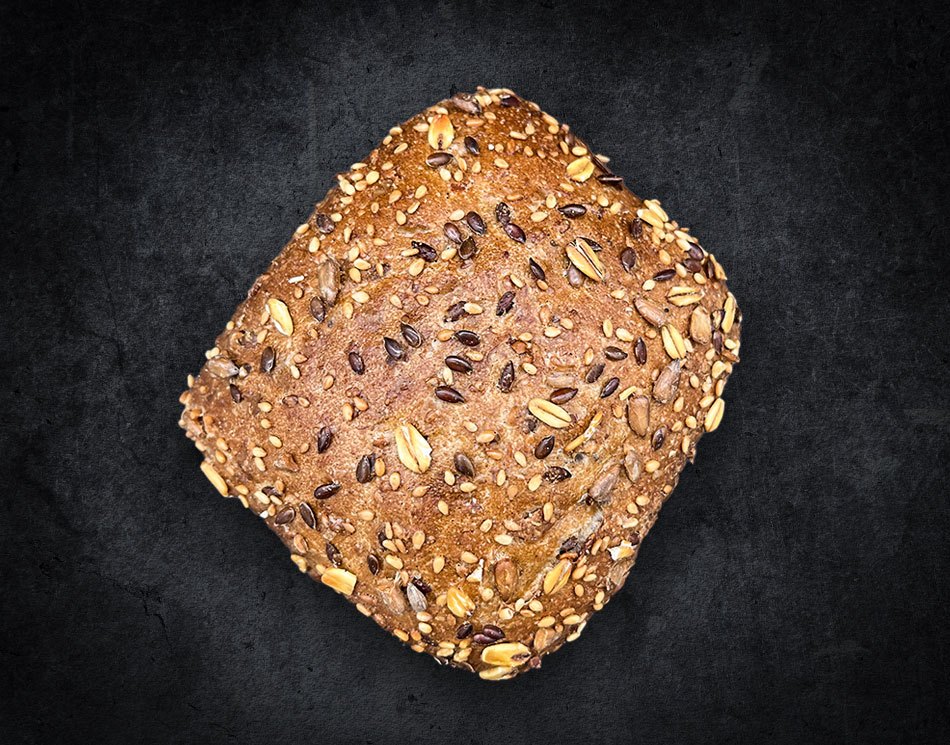 Ein Mehrkorn-Brötchen mit verschiedenen Körnern. Es ist goldbraun und eckig.