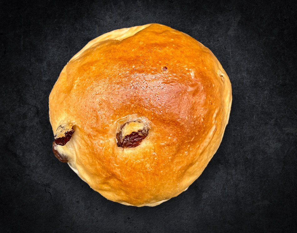Ein Rosinen-Wecken mit dunklen Rosinen. Es ist goldbraun und rund.
