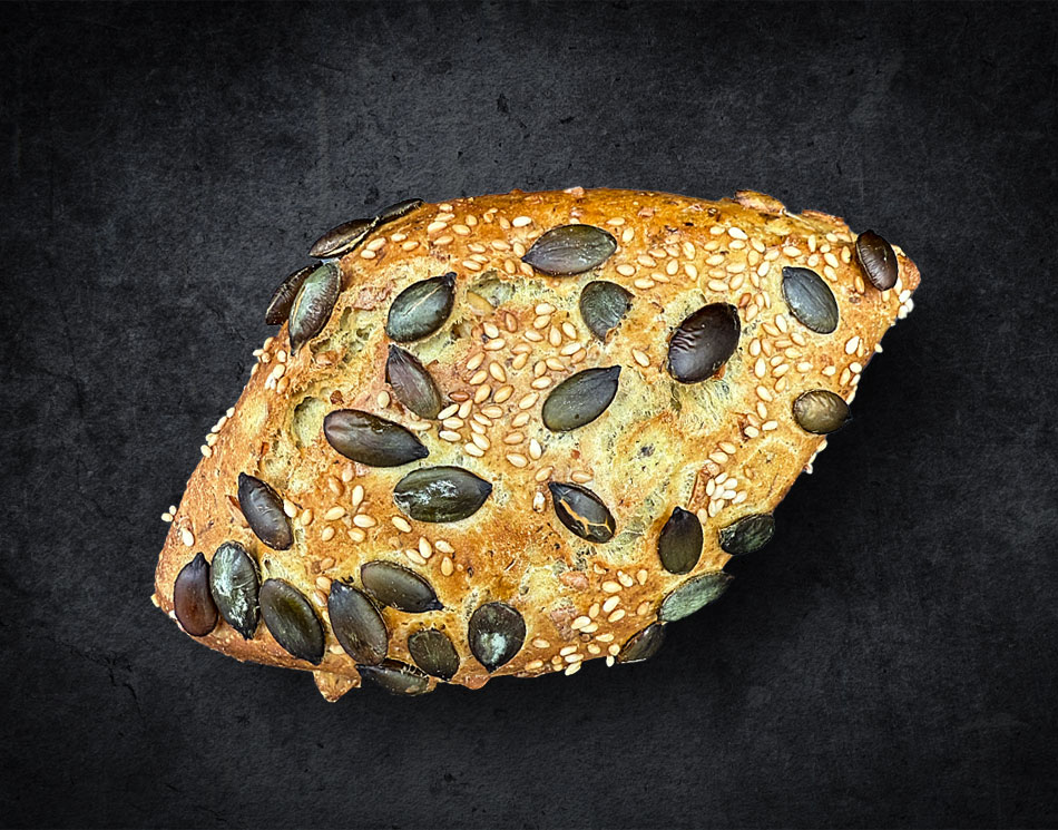 Ein Dinkel-Kürbis-Krüstchen mit Kürbis-Kernen. Es ist goldbraun und eckig.