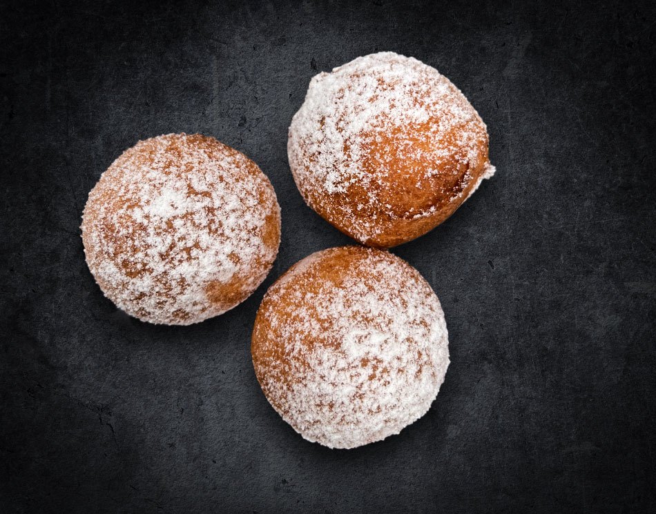 Drei kleine Quarkbällchen nebeneinander. Sie sind goldbraun gebacken und mit Puderzucker bestreut.