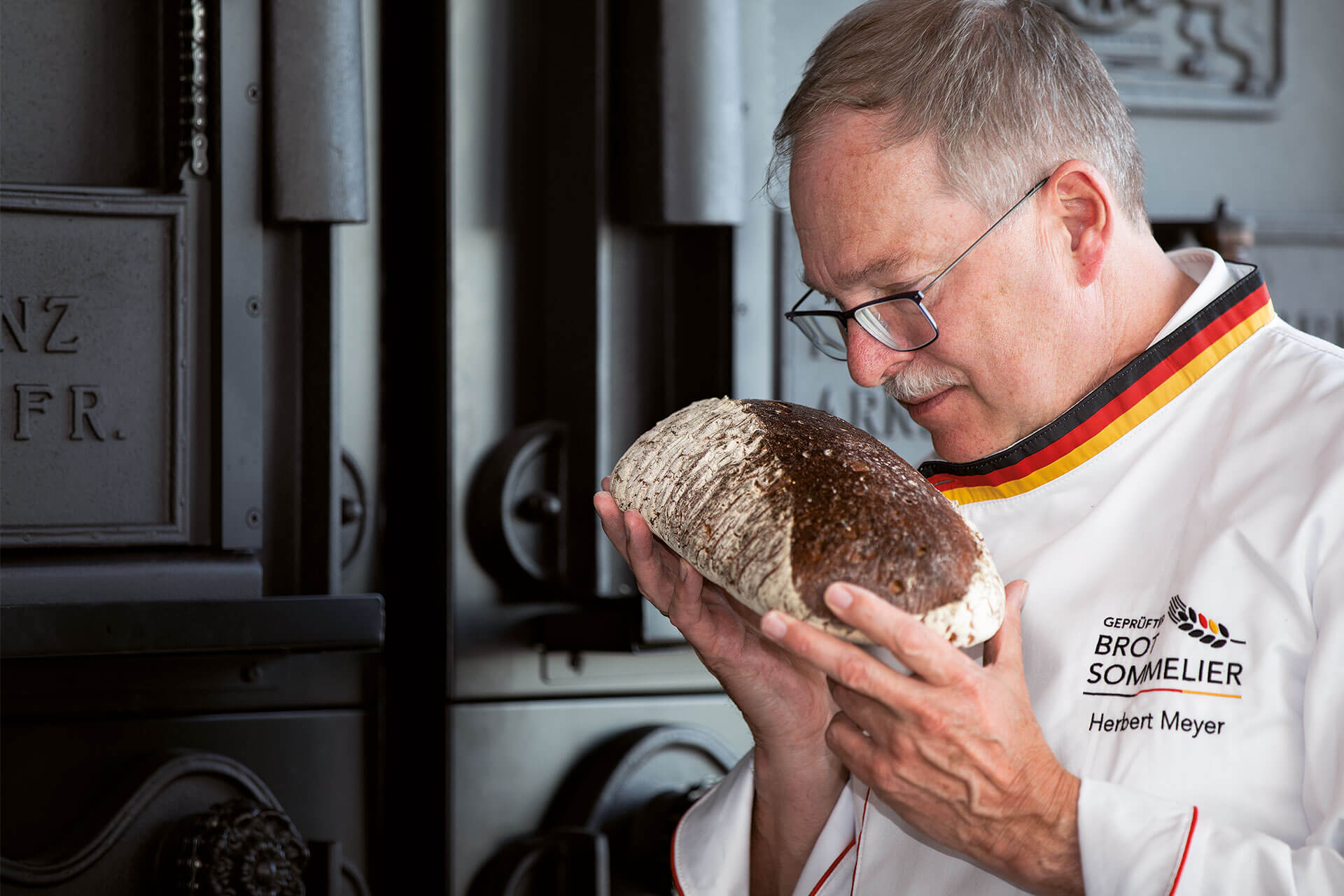 Herbert Meyer hält ein dunkles Brot. Er riecht an dem Brot. Er ist Brot-Sommelier.